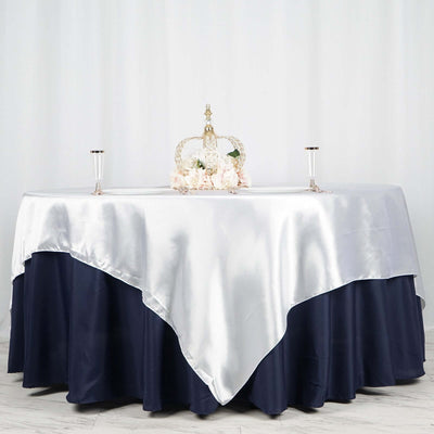Elegant table setup with silver and navy tablecloth, crown, and floral centerpiece.