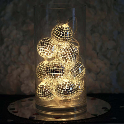 String lights in a glass vase with decorative disco ball ornaments.