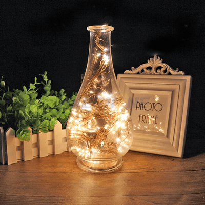 Decorative glass vase with fairy lights and greenery on a wooden table.