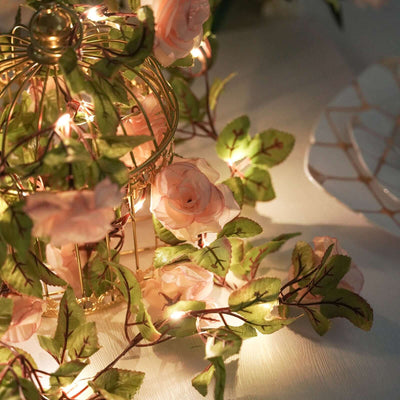 Decorative birdcage with fairy lights and pink roses on a table.