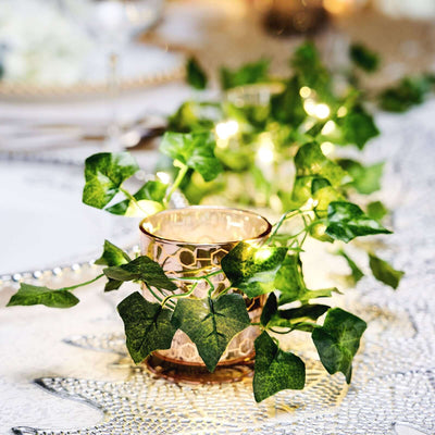 Decorative candle holder with ivy and fairy lights on a table setting.