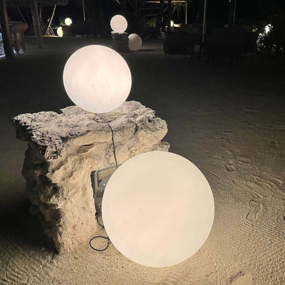 Illuminated round outdoor lights on a stone pedestal at night.