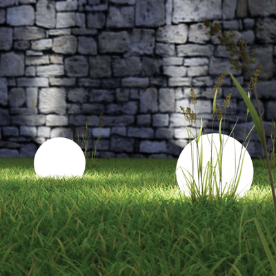 Glowing outdoor decorative spheres in grass against a stone wall backdrop.