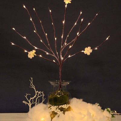 Decorative lighted branch centerpiece with flowers in a glass vase.