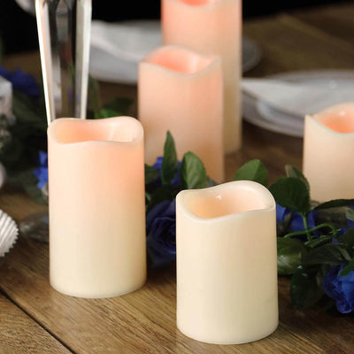 Flameless LED candles in varying heights on a wooden table with blue flowers.