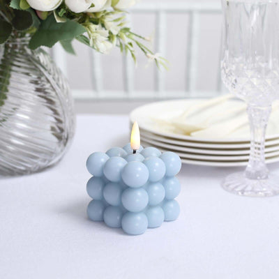 Blue bubble candle lit on a table with plates and floral arrangement.