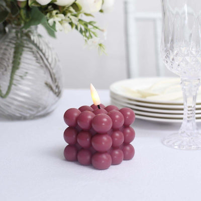 Bubble candle in burgundy color on a dining table with plates and glassware.