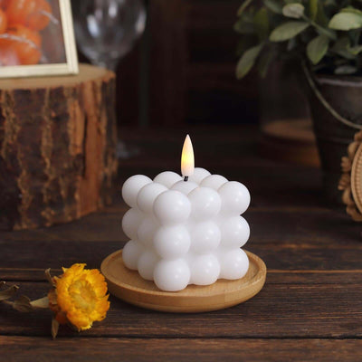 White bubble candle on a wooden plate with a flower, in a cozy setting.