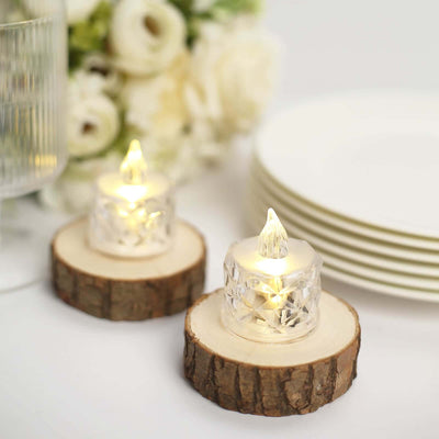Decorative LED candles on rustic wood slices with white plates and flowers in the background.