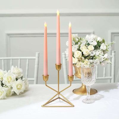Gold candle holder with three pink candles, elegant table setting with flowers.