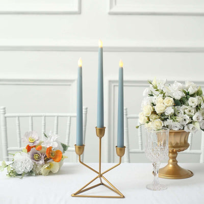 Elegant three-candle holder with blue candles and floral decor on a table.