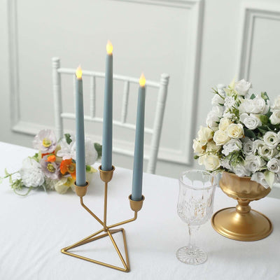 Three elegant candles in a stylish gold holder on a table with flowers.