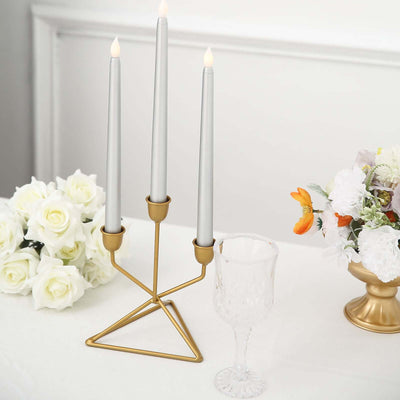 Elegant three-arm candle holder with silver candles, surrounded by flowers and glassware.