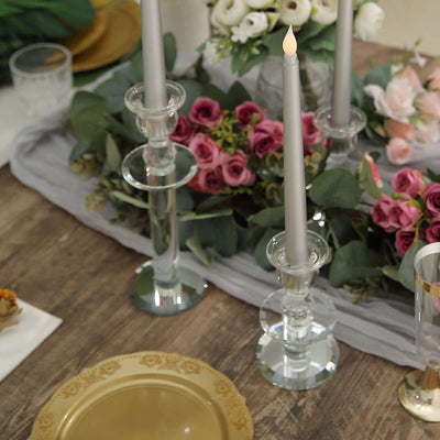 Elegant candle holders with gray candles and floral arrangement on a wooden table.
