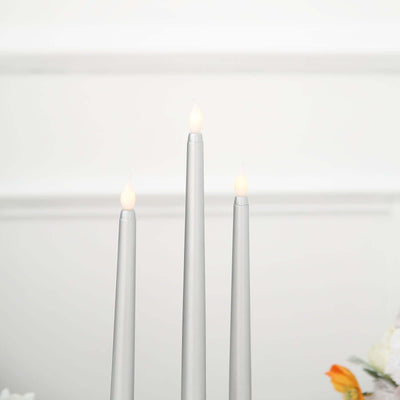 Silver taper candles with flame, arranged in a decorative setting.