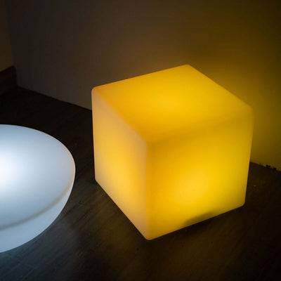 Yellow glowing cube lamp on a modern surface.