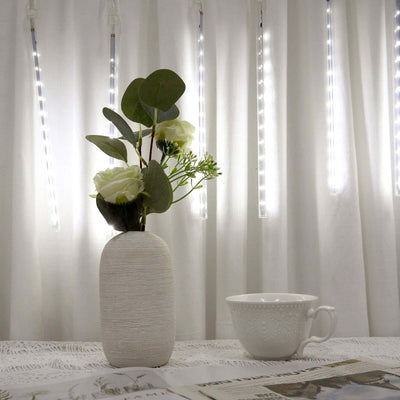 Vase with flowers and cup on a table against illuminated curtain backdrop.