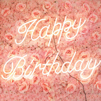 Neon "Happy Birthday" sign against a floral pink backdrop.