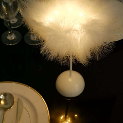 Elegant white feather lamp with soft lighting on a dark table setting.