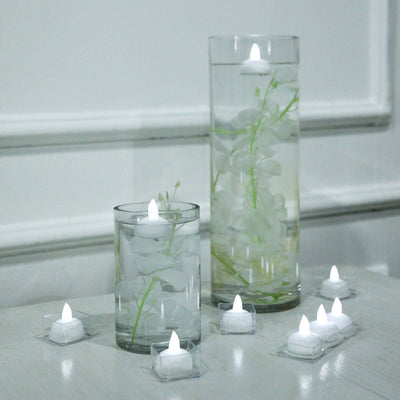 Floating LED candles in glass vases with greenery.