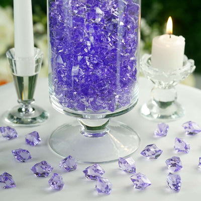 Purple decorative glass gems in a clear vase and scattered around a table.