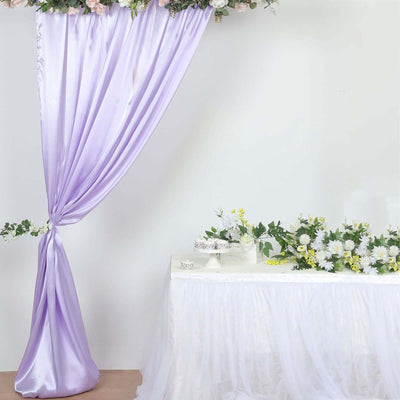 Purple drapery with flowers above a white table adorned with floral arrangements.
