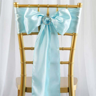Light blue satin chair sash with a bow and ring detail on a gold chiavari chair.
