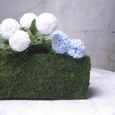 Artificial white and blue flowers in a moss-covered planter.
