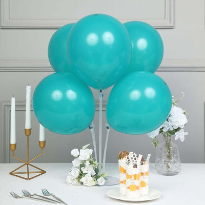 Teal balloons arranged with a dessert and flowers on a table.