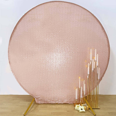Rose gold sequin backdrop with gold candle holders and candles on a wooden floor.