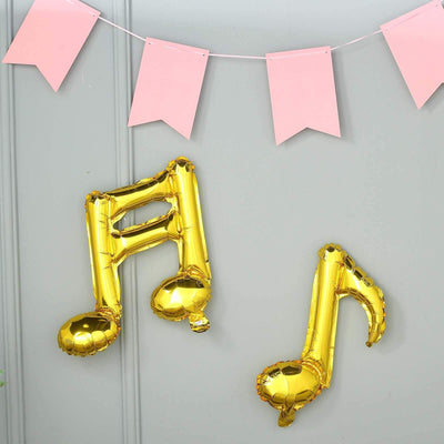 Gold musical note balloons hanging on a wall with pink bunting.