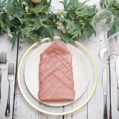 Elegant pink napkins arranged on a plate with greenery and tableware.