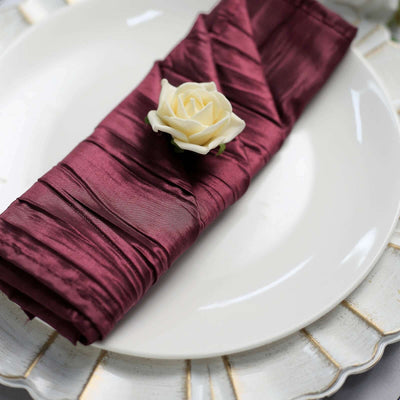 Burgundy satin napkin elegantly folded with a white rose on a decorative plate.
