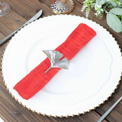 Red napkin with silver ginkgo leaf napkin ring on an elegant plate.