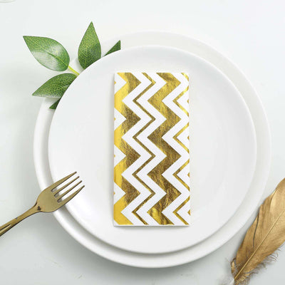 Gold chevron patterned napkin on white plates with greenery and a gold fork.