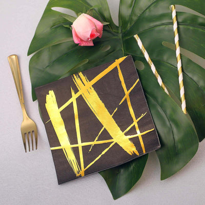 Black napkin with gold geometric design, gold fork, rose, and striped straws.