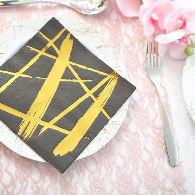 Black and gold decorative napkin on a white plate with a pink lace tablecloth.