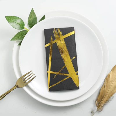 Black and gold decorative chocolate bar on white plates with greenery and a gold fork.