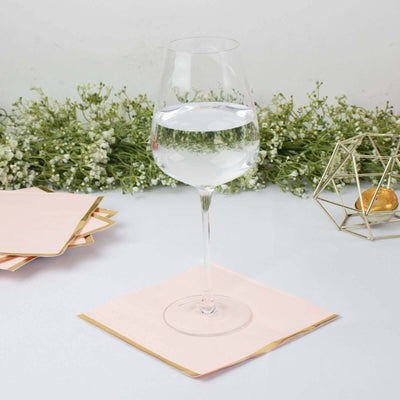 Clear wine glass with water on a pink napkin, surrounded by greenery.