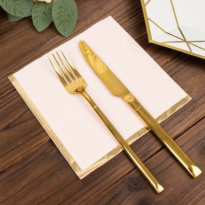 Gold cutlery set on a pink napkin with gold trim against a wooden background.
