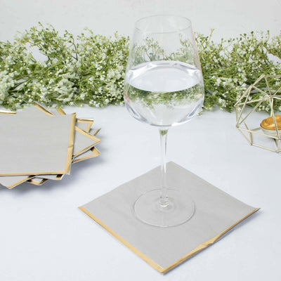 Elegant glass of water on a gold-trimmed gray napkin with floral decor.