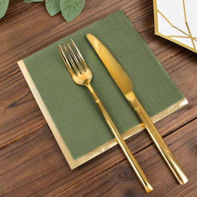 Gold knife and fork on a green napkin with a gold trim on a wooden table.