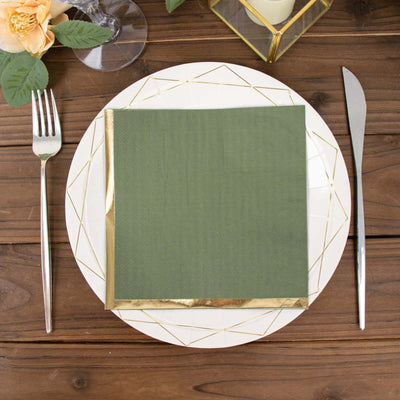 Green napkin with gold trim on a plate, set on a wooden table.