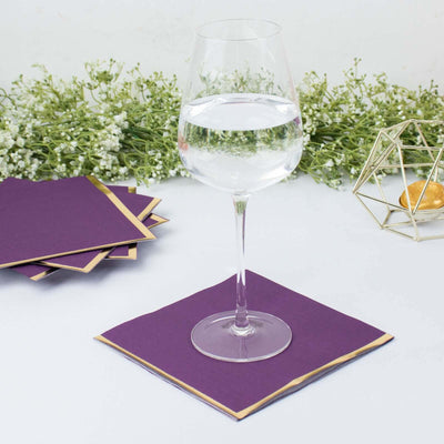 Glass of water on a purple napkin with decorative greenery in the background.