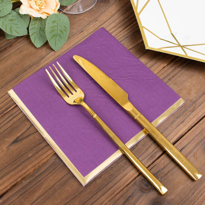 Gold cutlery on a purple napkin with a gold trim, set on a wooden table.