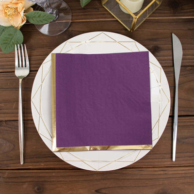Purple napkin with gold trim on a decorative plate, set on a wooden table.