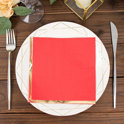 Red napkin with gold trim on a decorative plate, fork and knife on a wooden table.