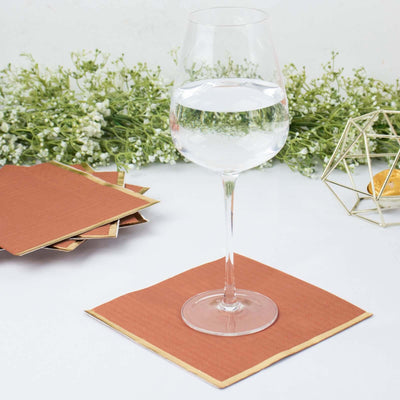 Glass of water on a brown paper coaster with decorative greenery in the background.