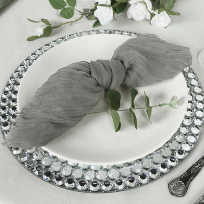 Gray napkin tied with greenery on a decorative plate with rhinestone border.