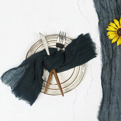 Table setting with a dark linen napkin, cutlery, and a sunflower on a plate.